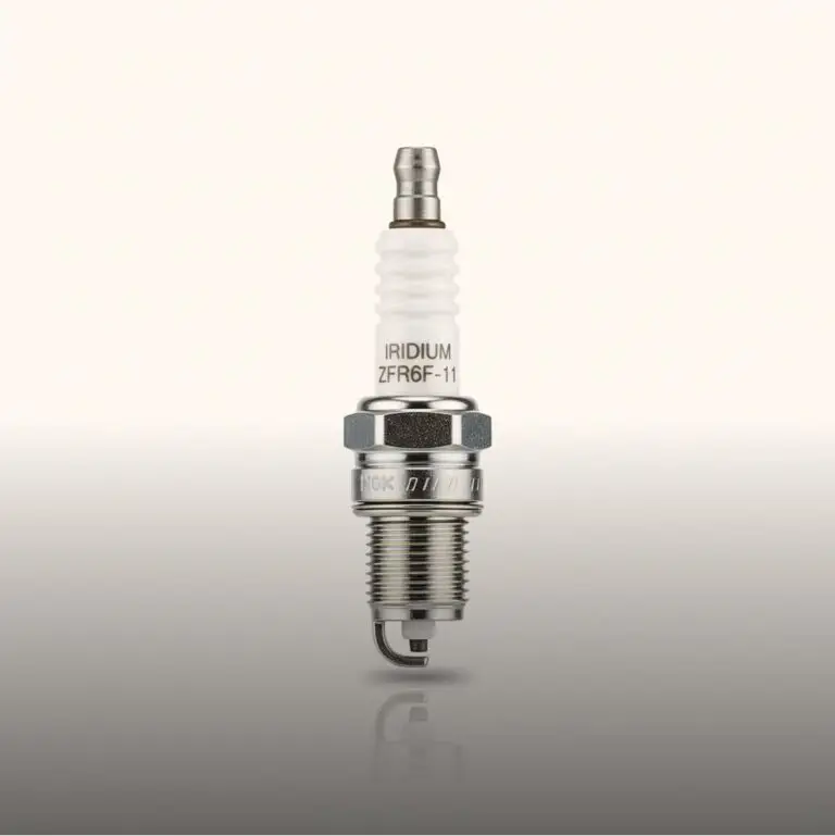 Vela de ignição da marca NGK Iridium em um fundo cinza claro. O corpo da vela é branco e o eletrodo e a rosca são metálicos.
