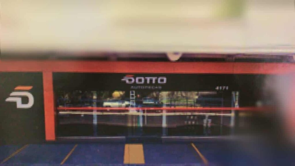Vista frontal de uma loja Dotto Autopeças com a nova identidade visual. A fachada em laranja e preto tem o logo da marca e uma grande vitrine de vidro.
