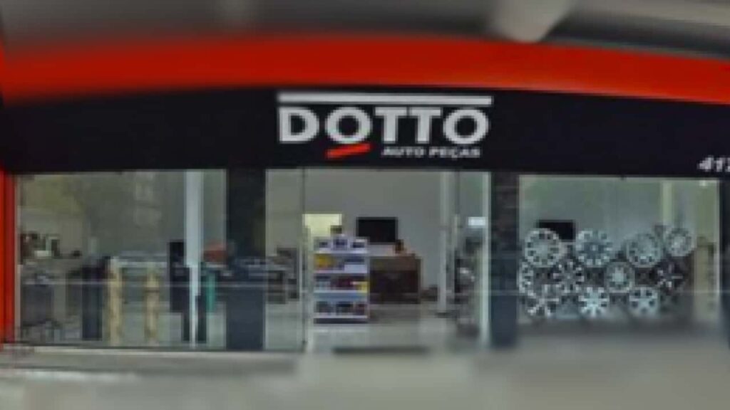 Fachada moderna da loja "DOTTO AUTOPEÇAS". O letreiro é grande e chamativo, com as cores da marca, laranja e preto, e uma entrada de vidro.