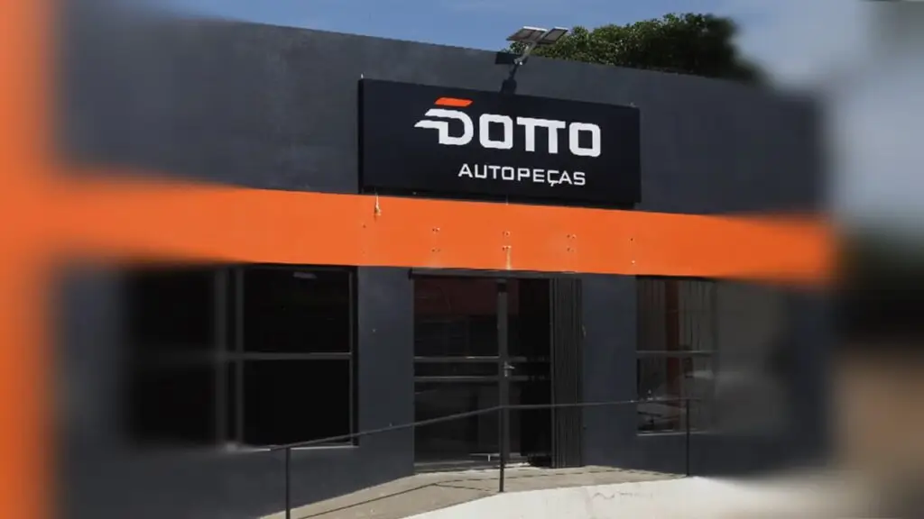 achada da loja Dotto Autopeças em Itaqui. O prédio cinza tem uma faixa laranja e um grande letreiro preto com o nome da empresa em branco.