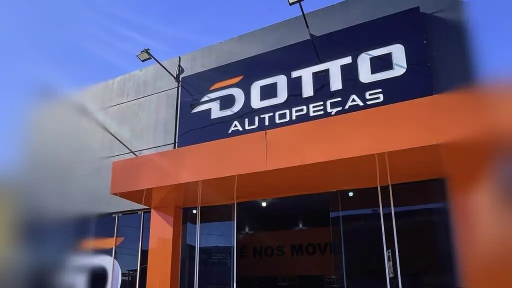 Vista da fachada da loja Dotto Autopeças em Quaraí. O letreiro da marca e o design em laranja e preto se destacam sob o céu azul.