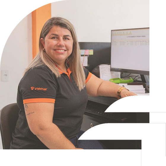 Colaboradora da Dotto Autopeças sorrindo, sentada à mesa de trabalho com um computador. A imagem tem bordas curvas.